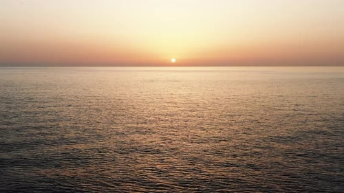 Drone Flying Backwards From Atmospheric Sunset Over Rippled Sea with Birds Flying Around
