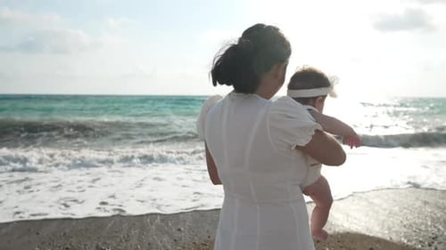 Back View of Asian Young Mother with Baby Daughter Admiring Sunset with Sunlight Reflecting in