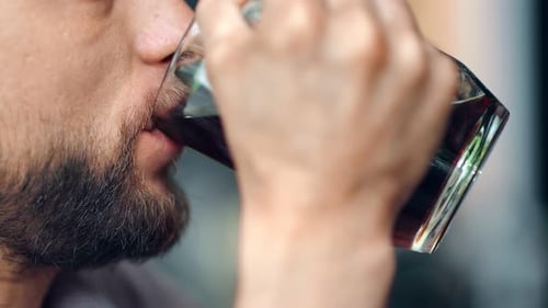 Extremer Männermund mit Bart und Schnurrbart, der erfrischendes Craft Beer aus einem Glasbecher trinkt