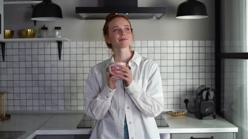 Retrato de una mujer pelirroja satisfecha con ropa casual tomando café en la cocina a cámara lenta