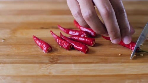 Hands chop fresh chili peppers with serrated knife