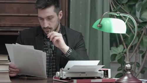 Writer Reads Manuscript by Typewriter Under Lamp