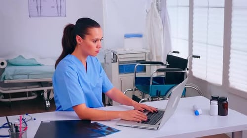 Woman in Scrubs Typing on Laptop in Hospital