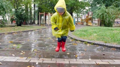 Slow Motion Video of Cheerful Little Boy in Raincoat and Wellington Boots Jumping in Puddle and