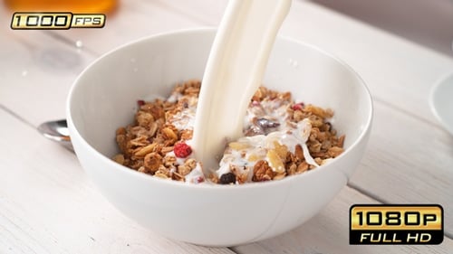 Pouring Milk Over Crunchy Granola in Bowl