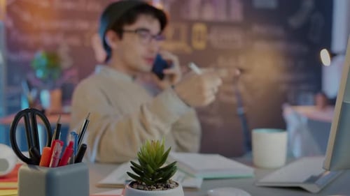 Blurred Young Businessman Speaking on Mobile Phone Working Late in Creative Office