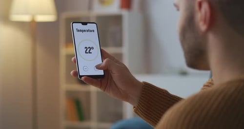 Man Is Controlling and Adjusting Smart Home System By App in Smartphone Closeup View of Gadget
