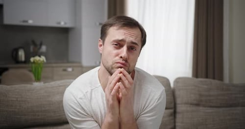Man Sits on Couch with Sad Expression