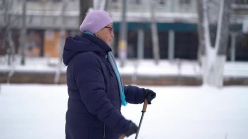 Senior Woman Walks in the Snow with Sticks