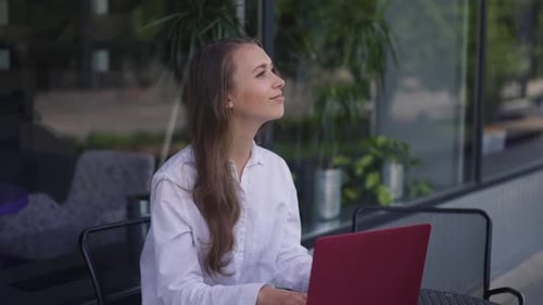 Young Positive Woman Sitting at Table with Laptop Greeting Friend Meeting in Sidewalk Cafe Outdoors