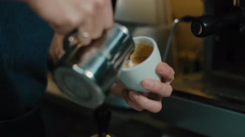 Barista making latte art in specialty coffee shop. Professional man making pouring stream milk