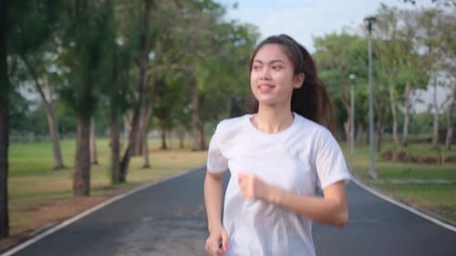 Portrait of Asian sport woman is jogging on road in green park with evening light and happy emotion