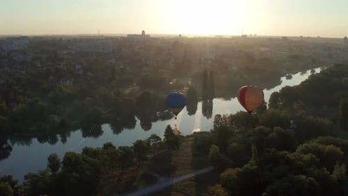 Beautiful flight at the sunrise of a red balloon over a river, forest, green trees.