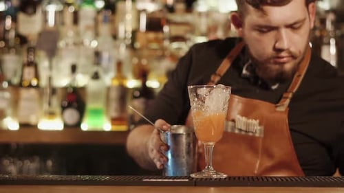 Close Shot at the Bartender's Hands a Man Pours a Cocktail From a Shaker Into a Glass