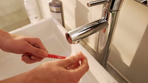 Man washing his toothbrush under sink in bathroom