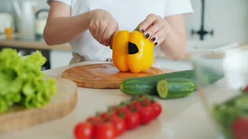Close-up of Girl's Hand Cutting Pepper on Wooden Board Using Knife Cooking Salad