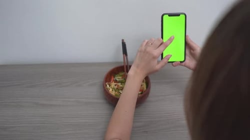 A Woman Using Smartphone With Green Touch Screen While Eating At Home