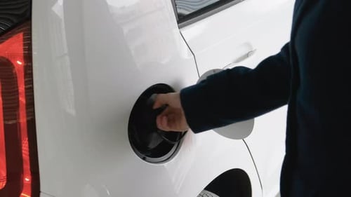 Geschäftsfrau beim Einstecken eines Ladegeräts in das Elektroauto an der Ladestation im Parking and Go