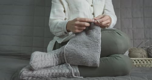 Woman knitting wool clothing on couch