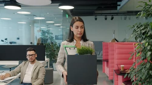 Sad Young Woman Leaving Work with Box of Stuff Walking in Open Space Office
