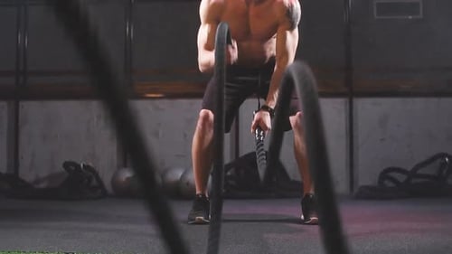 Hombre guapo, musculoso, con el pecho desnudo, con cuerdas de batalla, ejercicio en el gimnasio. Cámara lenta