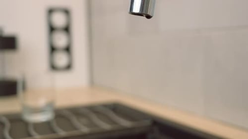 Water Droplets Dripping from Silver Faucet into Sink