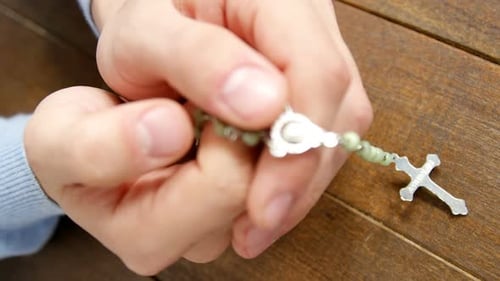 Hands Holding Rosary Beads on a Wooden Table
