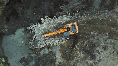 Large yellow excavator or bulldozer takes stones with bucket and fills hole.