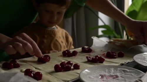 Child and Adult Putting Cherries on Dough
