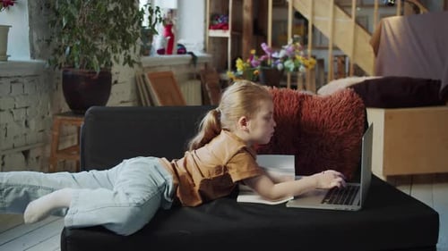 The Girl Lies on the Couch and Looks for Something in the Browser on the Laptop