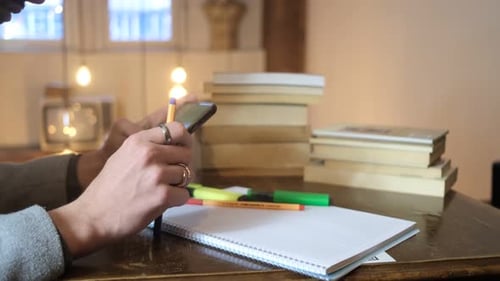 Person Uses Phone at Desk with Notebook and Books