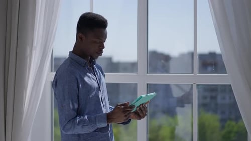 Young Adult Using Tablet Device by Window