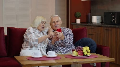 Senior Couple Using Smartphone Together on Sofa