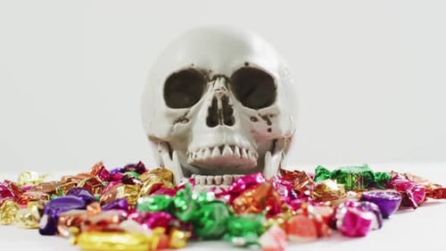 Close up view of human skull and multiple candies fallen against grey background