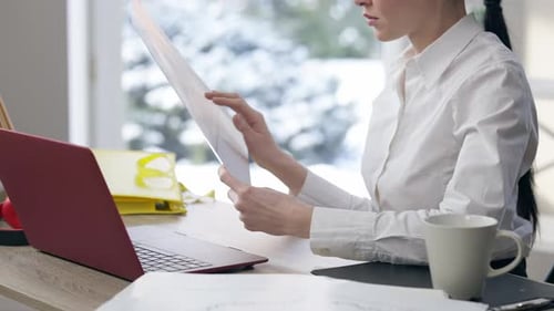 Analista irreconhecível analisando documentos sentados com laptop em ambientes fechados no escritório