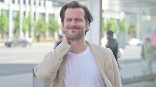 Man Rubbing Neck in Discomfort on City Street