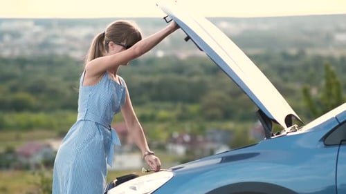 Young Female Driver Standing Alone Near a Broken Car with Popped Up Hood Inspecting Her Vehicle