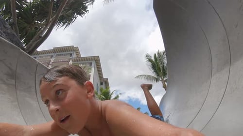 A boy plays on a waterslide water slide in a pool at a hotel resort.