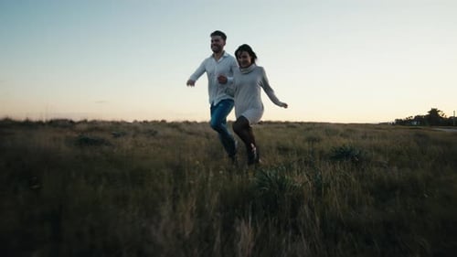 Couple Running Through Field at Sunset