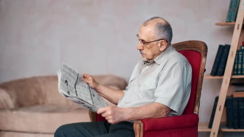 Focused Elderly Man Studying Interesting Newspaper Media Publication on Vintage Armchair at Home
