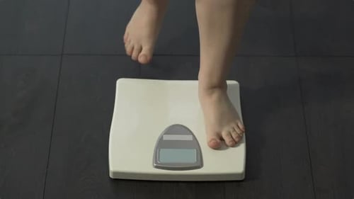 Weibliche Tritte auf Hauswaage, um Gewicht, Fettleibigkeit und Gesundheitsprobleme zu messen