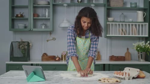 Young Woman Kneading Dough in Kitchen with Tablet