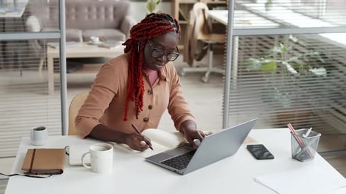 Female Manager Working on Computer and Writing in Notepad
