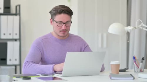 Man Smiling While Typing on Laptop at Desk