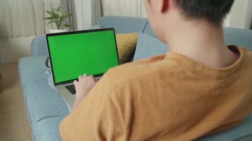Male Using Laptop With Green Screen In Living Room