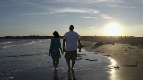Romantic Couple Holding Hands While Walking On The Beach At Sunset. - rear, tracking shot