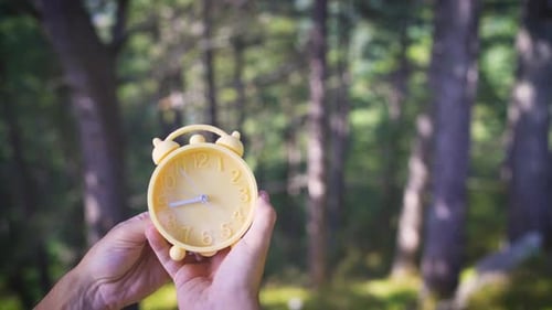 Hands Holding Clock in Forest with Time Moving Quickly