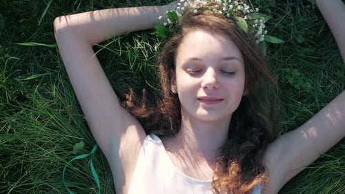 SLOW MOTION: Top view shot of a Caucasian girl in a white floral dress lying in grass