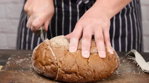 Person Slicing Fresh Bread on Cutting Board