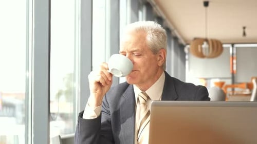 Senior Businessman Looks Out the Window at the Cafe